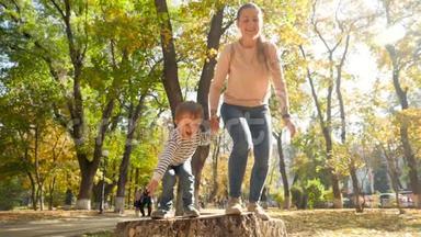 欢快的小男孩手牵着妈妈从<strong>秋天</strong>公园的树桩上跳下来的慢动作<strong>视频</strong>
