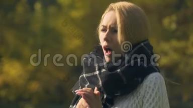 戴围巾的患病妇女在秋季公园咳嗽和打喷嚏，感冒，免疫