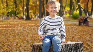 慢动作视频快乐的微笑和笑的男孩坐在树桩上，向树桩投掷黄色和橙色的叶子