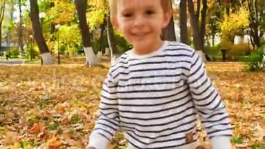 4k<strong>视频</strong>：微笑的幼儿男孩在<strong>秋天</strong>公园捡黄叶，并把它们扔进照相机