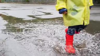 慢动作特写视频，儿童穿红色橡胶靴在公园的大水坑上行走，溅水。 儿童
