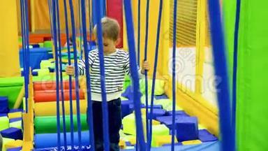 在游乐园儿童游乐场里，小男孩在摇晃的绳桥上行走