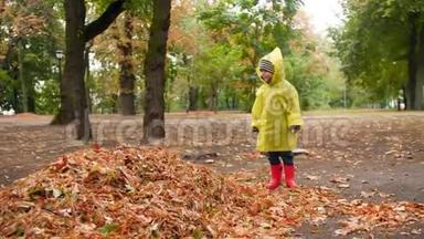 4k视频快乐快乐的小男孩穿着橡胶靴和雨衣在秋天的落叶堆里跳跃
