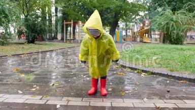 4k慢动作视频：穿着雨衣和惠灵顿靴子的快乐小男孩在水坑里跳，在水中泼水
