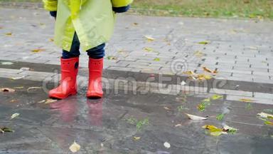 儿童穿红色橡胶<strong>惠</strong>灵顿靴子和雨衣在大水坑里跳跃和行走的4k特写慢<strong>动</strong>作视频