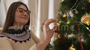 穿着圣诞毛衣，微笑着装饰圣诞树挂玩具的年轻幸福女子