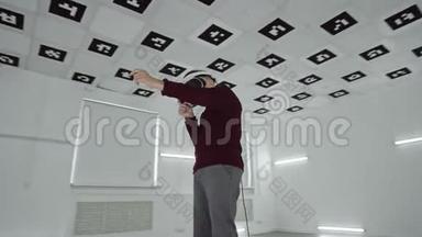 穿着棕色毛衣的小男孩正在虚拟现实中玩射击游戏，他在空荡荡的游戏室里戴着耳机
