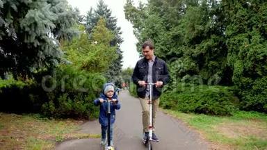 快乐的年轻父亲和小儿子在秋天公园骑滑板车的视频。 一家人玩得开心