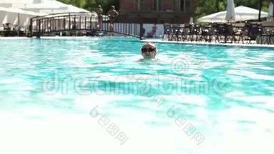 美丽的年轻女子戴着太阳镜游泳，双手走上泳池边，兴高采烈地看着相机。