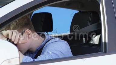 年轻人在交通堵塞中很累。 他把头放在方向盘上，坐在白色的蓝屏车上