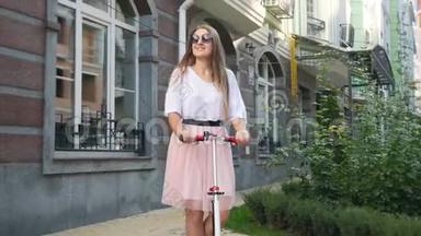 4k视频美丽的微笑女子穿着粉红色裙子骑在城市街道上使用滑板车