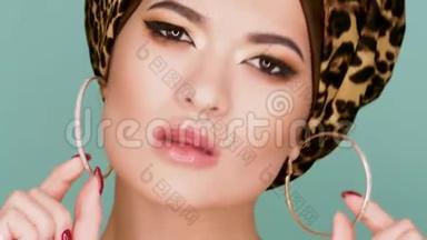 一个漂亮的年轻女子，戴着一顶由豹纹织物制成的时尚头巾，背景是蓝色。