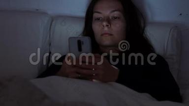 晚上躺在床上的年轻女人使用智能手机。 失眠和数字依赖，躺在床上的女孩