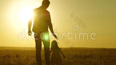 小女儿和爸爸牵着手在田野里走来走去。 孩子握着父亲`手。 一家人晚上步行出城