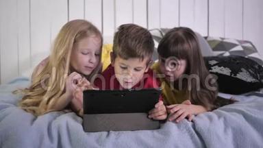 快乐的现代<strong>小朋友</strong>穿着多种颜色的t恤，使用平板电脑，躺在床上交流