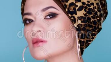 一个漂亮的年轻女子，戴着一顶由豹纹织物制成的时尚头巾，背景是蓝色。