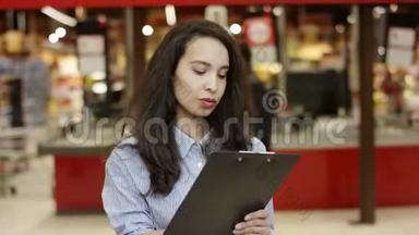 超市里漂亮的女孩在她的文件夹上写下<strong>信息</strong>，列出数字，做笔记，关闭视图
