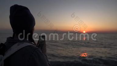 一个旅游女孩在手机上拍照日落。 日落时的剪影。
