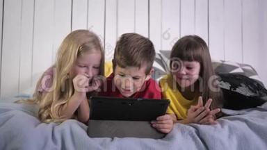 现代童年时代，穿着多种颜色t恤的小伙伴在<strong>家</strong>里躺在床上时使用<strong>数码</strong>平板电脑聊天