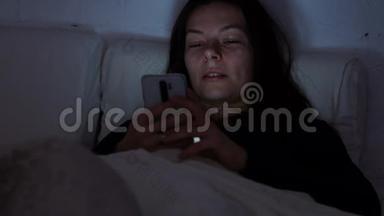 晚上躺在床上的年轻女人使用智能手机。 失眠和数字依赖，躺在床上的女孩