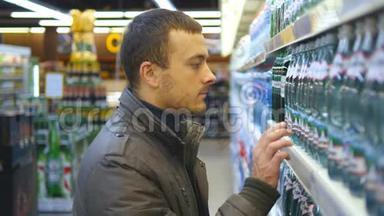 年轻人在<strong>超市</strong>里选择和购买一瓶矿泉水。 从<strong>杂货</strong>店货架上拿产品的家伙