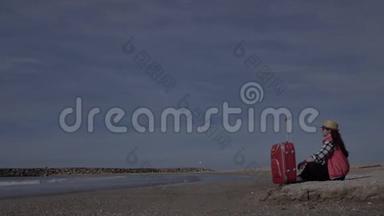 女游客带着一个手提箱坐在海边的海岸线上，在埃宁，旅游理念，复制空间。