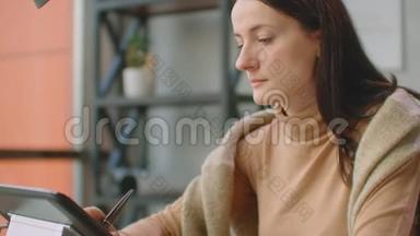 年轻的女人坐在她的办公桌前，她在画画，写作，用钢<strong>笔</strong>与数字平板电脑。 手<strong>拿笔</strong>。