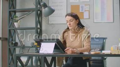 年轻的女人坐在她的办公桌前，她在画画，写作，用钢<strong>笔</strong>与数字平板电脑。 手<strong>拿笔</strong>。