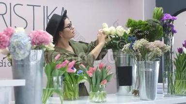 鲜花店。 戴帽子的欧洲女孩在商店的花瓶里仔细地调整花。