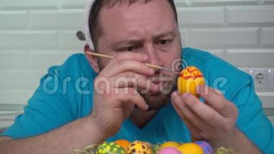 复活节快乐。 一个穿着兔子耳朵蓝色t恤的男人在厨房里画准备复活节的鸡蛋。