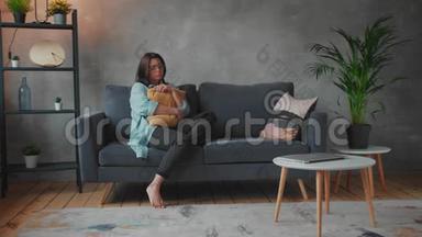 一个年轻的女孩坐在沙发上抱着枕头。 沮丧和沮丧的女人。 社会录像