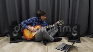 人类调谐电吉他。 戴耳机的人一边坐在客厅的地板上一边用笔记本调吉他。 年轻<strong>教授</strong>
