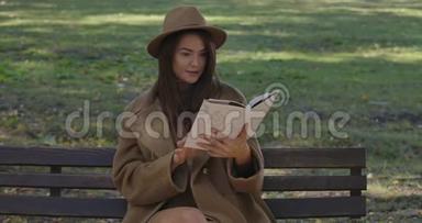 可爱的高加索女学生穿着优雅的棕色衣服坐在长凳上翻书页。 聪明的人