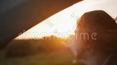 在大自然中日落。 女人在车里，手在空中玩耍。 阳光穿过树木. 风吹头发。 慢节奏