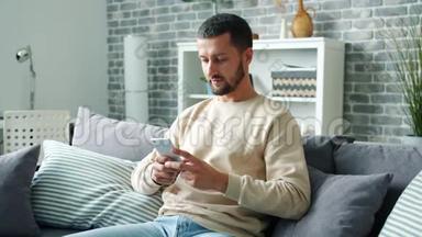 可爱的长胡子男人用智能手机发短信，独自在家里开心地微笑