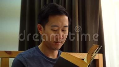 一幅30多岁的亚洲男人的肖像，穿着休闲服，在家里躺在床上看书。娱乐和