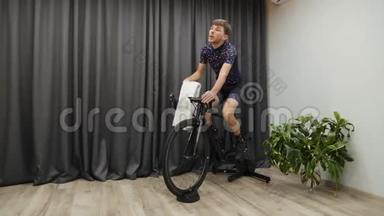 室内自行车教练的专业自行车训练。 男<strong>运动</strong>员在家骑自行车，<strong>出汗</strong>，手拿毛巾和