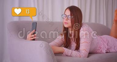 在社交媒体上，戴眼镜的可爱白种人女孩在沙发上躺着手机<strong>获得</strong>了人们的喜爱