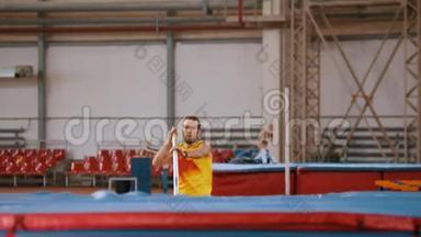 撑杆跳-穿黄色T恤的高个子运动员在酒吧里奔跑跳跃