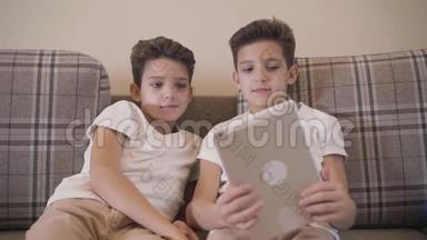 前景特写两个高加索双胞胎兄弟看着平板电脑屏幕微笑。 小兄弟靠在