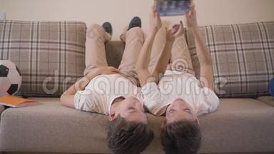 两个快乐的高加索<strong>双胞胎兄弟</strong>躺在沙发上用平板电脑。 小<strong>兄弟</strong>在家里一起休息。 儿童