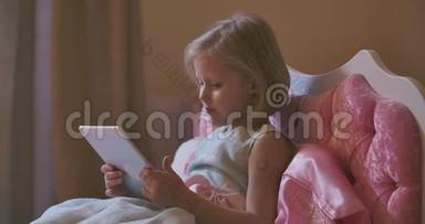 <strong>漂亮</strong>的金发白种人女孩躺在粉红色的床上用平板电脑的肖像。 现代儿童在看动画片之前