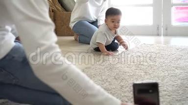家长用智能手机拍摄可爱的亚洲宝宝在家里柔软的白地毯上爬行的视频