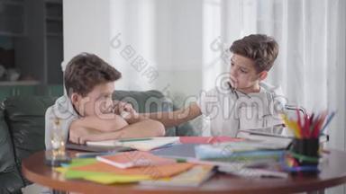 可爱的白种人男孩醒来，他的孪生兄弟坐在桌子旁。 小兄弟在家一起做作业