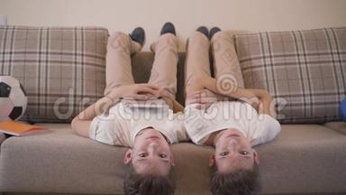 两个高加索<strong>双胞胎兄弟</strong>倒躺在沙发上，看着摄像机笑着。 快乐的<strong>兄弟</strong>姐妹