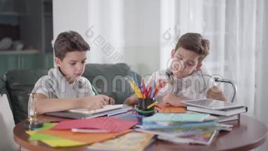 两个富有创造力的高加索<strong>双胞胎兄弟</strong>坐在桌子旁，用五颜六色的铅笔画画。 可爱的男孩看着他的<strong>兄弟</strong>