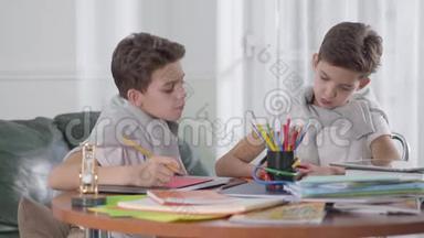 两个高加索双胞胎兄弟坐在桌子旁学习。 一个男孩试图作弊，他的兄弟关闭了他的锻炼