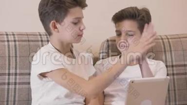 白种人双胞胎兄弟在平板电脑上玩电子游戏和击掌的特写镜头。 小兄弟玩得开心