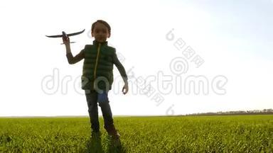 一个快乐快乐的男孩跑过一片绿色的草地，手里拿着一架飞机。 日落背景下快乐的孩子。