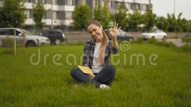 手势好的！ 远射。 20岁的女孩穿着格子衬衫坐在草地上，真诚地笑了